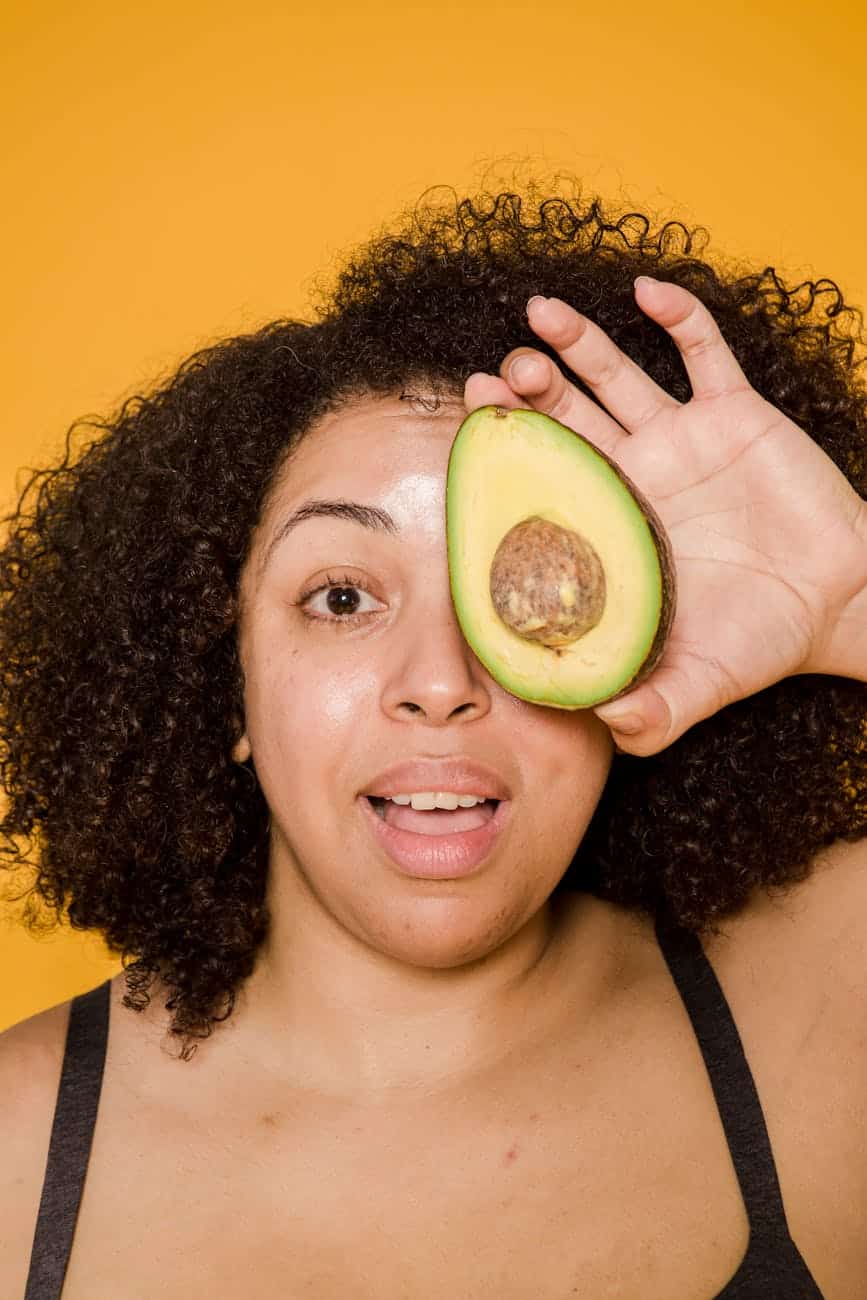 Surprised Ethnic Model With Fresh Avocado Half And Afro Hairstyle